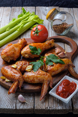 Baked chicken legs and wings lie on the table. Nearby are cherry tomatoes, celery, parsley and spices.