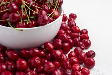 Fresh cherries in a white plate and scattered around on a light stone background