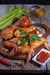 Baked chicken legs and wings lie on the table. Nearby are cherry tomatoes, celery, parsley and spices.