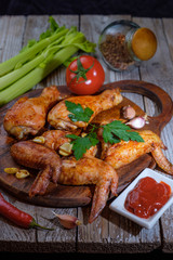 Baked chicken legs and wings lie on the table. Nearby are cherry tomatoes, celery, parsley and spices.