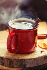 Mulled wine in a red ceramic mug over rustic wooden boards surrounded spices.