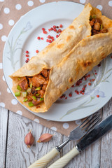 Doner kebab is lying on a white plate. Shawarma with meat, onions, salad lies on a white old wooden table.