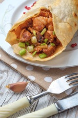 Doner kebab is lying on a white plate. Shawarma with meat, onions, salad lies on a white old wooden table.
