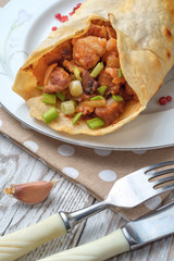 Doner kebab is lying on a white plate. Shawarma with meat, onions, salad lies on a white old wooden table.