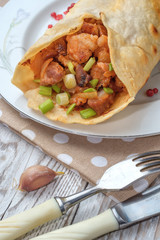 Doner kebab is lying on a white plate. Shawarma with meat, onions, salad lies on a white old wooden table.