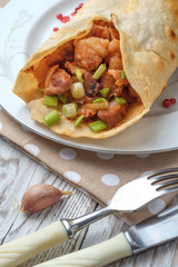 Doner kebab is lying on a white plate. Shawarma with meat, onions, salad lies on a white old wooden table.