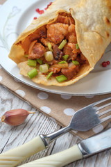Doner kebab is lying on a white plate. Shawarma with meat, onions, salad lies on a white old wooden table.