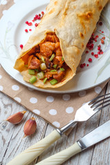 Doner kebab is lying on a white plate. Shawarma with meat, onions, salad lies on a white old wooden table.