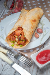 Doner kebab is lying on a white plate. Shawarma with meat, onions, salad lies on a white old wooden table.