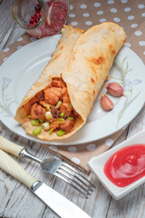 Doner kebab is lying on a white plate. Shawarma with meat, onions, salad lies on a white old wooden table.