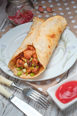 Doner kebab is lying on a white plate. Shawarma with meat, onions, salad lies on a white old wooden table.