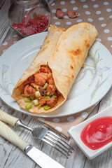 Doner kebab is lying on a white plate. Shawarma with meat, onions, salad lies on a white old wooden table.