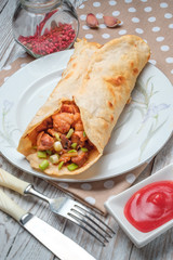 Doner kebab is lying on a white plate. Shawarma with meat, onions, salad lies on a white old wooden table.