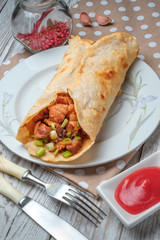 Doner kebab is lying on a white plate. Shawarma with meat, onions, salad lies on a white old wooden table.