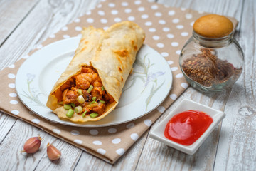 Doner kebab is lying on a white plate. Shawarma with meat, onions, salad lies on a white old wooden table.