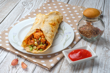 Doner kebab is lying on a white plate. Shawarma with meat, onions, salad lies on a white old wooden table.
