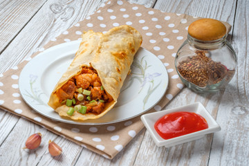 Doner kebab is lying on a white plate. Shawarma with meat, onions, salad lies on a white old wooden table.