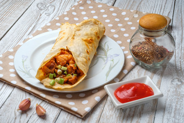 Doner kebab is lying on a white plate. Shawarma with meat, onions, salad lies on a white old wooden table.