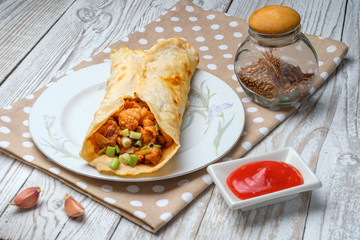 Doner kebab is lying on a white plate. Shawarma with meat, onions, salad lies on a white old wooden table.