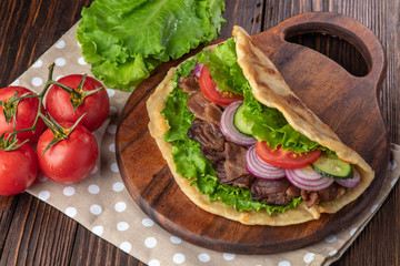 Delicious fresh homemade sandwich with chicken burspit roasted meat, tomato, onions and lettuce on wooden board on dark wooden table. Doner kebab. Healthy food concept.