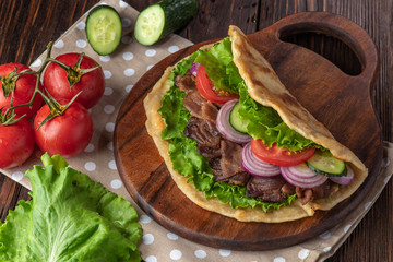 Delicious fresh homemade sandwich with chicken burspit roasted meat, tomato, onions and lettuce on wooden board on dark wooden table. Doner kebab. Healthy food concept.