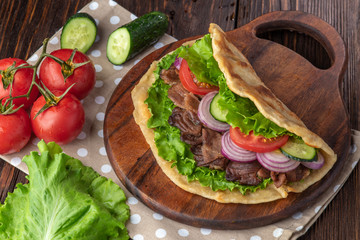 Delicious fresh homemade sandwich with chicken burspit roasted meat, tomato, onions and lettuce on wooden board on dark wooden table. Doner kebab. Healthy food concept.