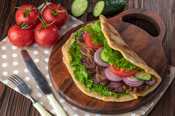 Delicious fresh homemade sandwich with chicken burspit roasted meat, tomato, onions and lettuce on wooden board on dark wooden table. Doner kebab. Healthy food concept.