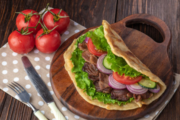 Delicious fresh homemade sandwich with chicken burspit roasted meat, tomato, onions and lettuce on wooden board on dark wooden table. Doner kebab. Healthy food concept.