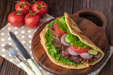 Delicious fresh homemade sandwich with chicken burspit roasted meat, tomato, onions and lettuce on wooden board on dark wooden table. Doner kebab. Healthy food concept.