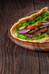 Delicious fresh homemade sandwich with chicken burspit roasted meat, tomato, onions and lettuce on wooden board on dark wooden table. Doner kebab. Healthy food concept.