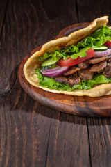 Delicious fresh homemade sandwich with chicken burspit roasted meat, tomato, onions and lettuce on wooden board on dark wooden table. Doner kebab. Healthy food concept.