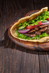 Delicious fresh homemade sandwich with chicken burspit roasted meat, tomato, onions and lettuce on wooden board on dark wooden table. Doner kebab. Healthy food concept.