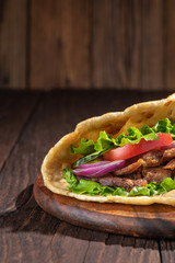 Delicious fresh homemade sandwich with chicken burspit roasted meat, tomato, onions and lettuce on wooden board on dark wooden table. Doner kebab. Healthy food concept.