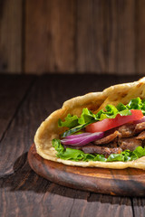 Delicious fresh homemade sandwich with chicken burspit roasted meat, tomato, onions and lettuce on wooden board on dark wooden table. Doner kebab. Healthy food concept.