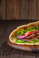Delicious fresh homemade sandwich with chicken burspit roasted meat, tomato, onions and lettuce on wooden board on dark wooden table. Doner kebab. Healthy food concept.