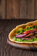 Delicious fresh homemade sandwich with chicken burspit roasted meat, tomato, onions and lettuce on wooden board on dark wooden table. Doner kebab. Healthy food concept.