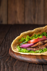 Delicious fresh homemade sandwich with chicken burspit roasted meat, tomato, onions and lettuce on wooden board on dark wooden table. Doner kebab. Healthy food concept.