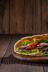 Delicious fresh homemade sandwich with chicken burspit roasted meat, tomato, onions and lettuce on wooden board on dark wooden table. Doner kebab. Healthy food concept.