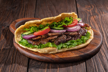 Delicious fresh homemade sandwich with chicken burspit roasted meat, tomato, onions and lettuce on wooden board on dark wooden table. Doner kebab. Healthy food concept.