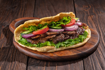 Delicious fresh homemade sandwich with chicken burspit roasted meat, tomato, onions and lettuce on wooden board on dark wooden table. Doner kebab. Healthy food concept.
