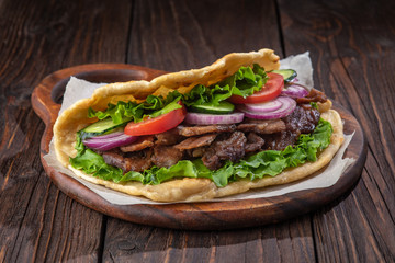 Delicious fresh homemade sandwich with chicken burspit roasted meat, tomato, onions and lettuce on wooden board on dark wooden table. Doner kebab. Healthy food concept.