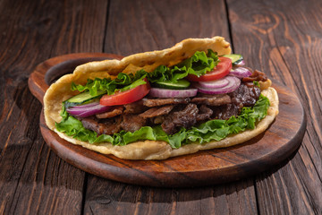 Delicious fresh homemade sandwich with chicken burspit roasted meat, tomato, onions and lettuce on wooden board on dark wooden table. Doner kebab. Healthy food concept.