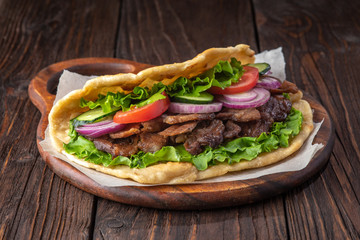 Delicious fresh homemade sandwich with chicken burspit roasted meat, tomato, onions and lettuce on wooden board on dark wooden table. Doner kebab. Healthy food concept.