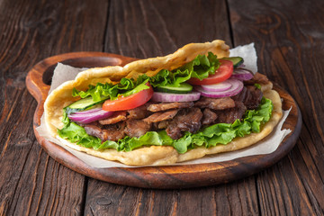 Delicious fresh homemade sandwich with chicken burspit roasted meat, tomato, onions and lettuce on wooden board on dark wooden table. Doner kebab. Healthy food concept.