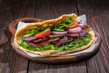 Delicious fresh homemade sandwich with chicken burspit roasted meat, tomato, onions and lettuce on wooden board on dark wooden table. Doner kebab. Healthy food concept.