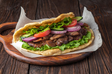 Delicious fresh homemade sandwich with chicken burspit roasted meat, tomato, onions and lettuce on wooden board on dark wooden table. Doner kebab. Healthy food concept.