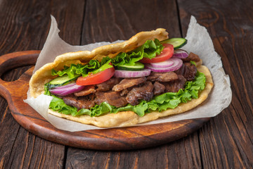 Delicious fresh homemade sandwich with chicken burspit roasted meat, tomato, onions and lettuce on wooden board on dark wooden table. Doner kebab. Healthy food concept.