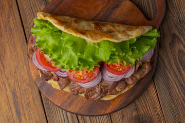 Delicious fresh homemade sandwich with chicken burspit roasted meat, tomato, onions and lettuce on wooden board on dark wooden table. Doner kebab. Healthy food concept.