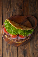 Delicious fresh homemade sandwich with chicken burspit roasted meat, tomato, onions and lettuce on wooden board on dark wooden table. Doner kebab. Healthy food concept.