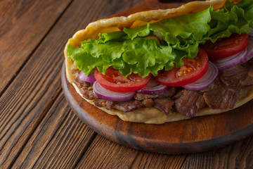Delicious fresh homemade sandwich with chicken burspit roasted meat, tomato, onions and lettuce on wooden board on dark wooden table. Doner kebab. Healthy food concept.